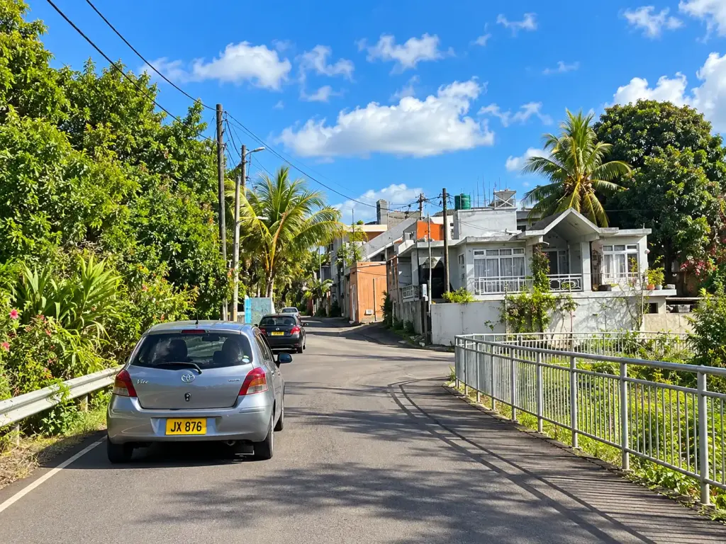 Typical narrow Mauritian village road with cars, motorcycles and local shops.